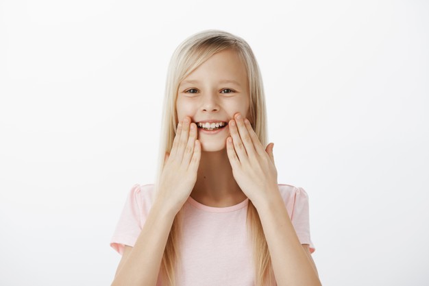pleased-grinning-adorable-child-with-blond-hair-smiling-broadly-holding-palms-near-lips-being-amazed-satisfied-with-healthy-teeth-attending-dentist-feeling-happiness_176420-22170